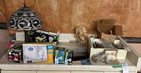 Full lot overview showing stained glass style table lamp, boxes of bulbs, and lamp accessories including crystals and harps.