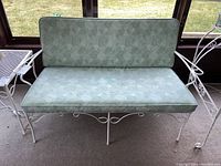Front view of loveseat showing green vinyl cushions with floral pattern on a white metal frame with paint chips.