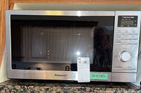 Front view of Panasonic Genius 1100W microwave oven showing digital control panel and stainless steel finish.