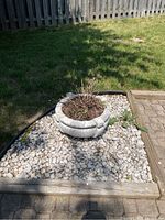 Concrete planter on a bed of white rocks in garden space near lawn and wood edging.
