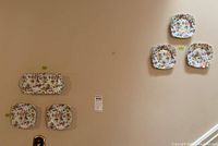 Five small square and round plates with colorful floral pavilion Lady-Gay pattern along with one rectangular platter mounted on wall.
