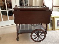 Side view of vintage solid wood tea trolley showing large spoked wooden wheels and caster wheels.