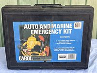 Closed black carrying case with label indicating Auto and Marine Emergency Kit by Carol including booster cables and trouble light.