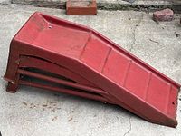 Two red metal ramps stuck together on concrete surface, showing wear and rust.