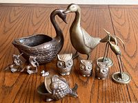 Photo of entire brass animal figurine collection including swans, duck, owls, fish, egrets, and unicorns on wooden table.