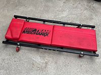 Top view of red padded vinyl car maintenance creeper with Team Mechanix logo and metal frame with caster wheels.