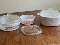 Three casserole dishes with lids on a wooden table, showing all three items together.