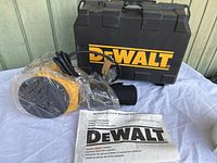 View of the DeWalt palm sander wrapped in plastic with the hard carrying case and instruction manual laid out on a table.