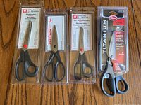 Four pairs of scissors in original packaging displayed on wooden surface.