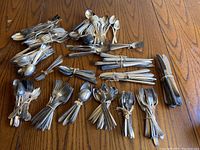Full view of large assortment of forks, spoons, and knives tied in bundles grouped on a wood surface.