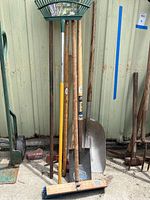 Full view of all yard tools showing a rake, shovels, axes, digging stick, and push broom leaning against wall.