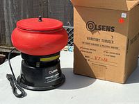 Photo showing front view of the Olsens VT-10 Vibratory Tumbler with red bowl and box next to it.