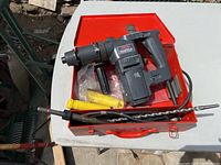 Overall view of the Skil Roto Hammer, drill bits, and carrying case on a white table outside.
