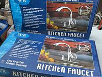 Two boxes of WaterRidge kitchen faucets showing packaging, product image and key features