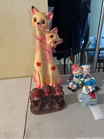 Four vintage ceramic piggy banks including tall cat with kitten, trio of monkeys, children on bench, and hippopotamus with rider