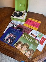 Vintage green RCA record player with cream tone arm and needle, hinge of lid broken, untested.