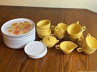 Full view of all items laid out on a wooden table including plates, yellow cups, creamers, sugar bowl, and saucers.