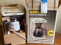 Front view of the vintage Norelco Dial-A-Brew II coffee maker in original box with cardboard inserts and plastic wrapping over the coffee pot and top of the machine.