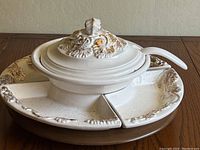 Full view of the soup tureen with lid and ladle placed on the wooden Lazy Susan, alongside four divided ceramic condiment dishes incorporated in the design.