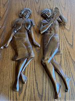 Pair of carved wooden dancing figures laid on wooden floor showing full length and pose details.