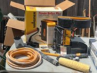 Photo showing Wagner Power Roller Plus painting system base unit, hose, roller handle, accessories, and packaging box in outdoor setting.