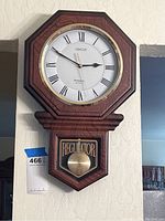 Full view of the Abacus battery operated wall regulator clock with wood grain finish and Roman numerals.