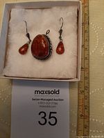 Front view of amber pendant/brooch and earrings inside jewelry box with ruler for size reference.