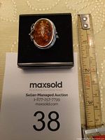 Top view of amber ring with silver leaf detail and measuring tape to show size approximation.