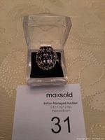 Top view of oval shaped ring with 7 amethyst stones in silver setting placed in clear box on auction paper