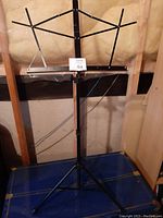 Black metal foldable music stand fully set up showing adjustable height and tripod base.