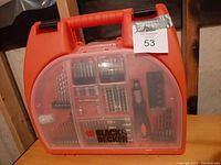 Closed red plastic carrying case with transparent lid revealing organized drill bits and accessories inside.