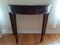 Front view of dark wooden half-moon table with tapered fluted legs and single drawer with two round metal handles.
