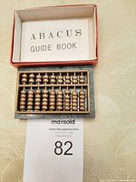 Photo of a small brass abacus resting in a green marble base, alongside an abacus guide book inside a red and white box.