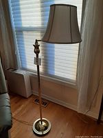 Full view of brass floor lamp positioned near window with lamp shade in place showing size and design.