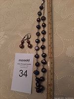 Full view of the pearl necklace with earrings alongside a ruler for size and auction lot number card.