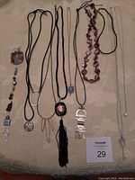 Full assortment of necklaces and pendants laid out on a fabric surface, showing variety of lengths and styles including chains, cords, and beads.