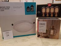 Box of bronze-finish flush mount light, box of Alice suspension fixture, and box of 4 Edison bulbs viewed from front.