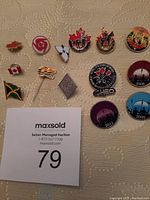 Image showing a variety of pins laid out on a beige surface with an auction card, including Canadian flags, symbolic pins, RCMP Musical Ride pins, and commemorative pins.