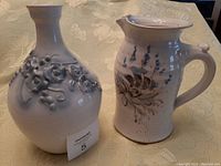 Front view of the pottery vase and jug on a floral tablecloth, showing their color and decorative details.