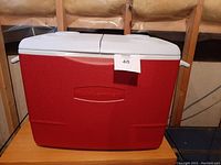 Front view of large red Rubbermaid cooler with white lid, showing brand embossing on front and handles on sides.