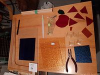 Full view of stained glass sheets, tools, and glass bits on wooden surface.