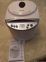 Front view of white Sunbeam breadmaker with closed lid, control panel and included user guide.