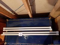 Four white spring rods, two approximately 36 inches and two approximately 40 inches, resting on a dark blue surface in a wooden framed space.
