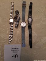 Four women's watches arranged on a textured surface showing variety of bands and face shapes.
