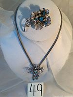 Overall view of the necklace and brooch set on a white display, showing the blue aquamarine stones and faux pearls.