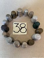 All 16 vintage sewing thimbles arranged in a circle on fabric background with a handwritten number 38 in the center.