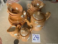 Stacked view of teacups, saucers, teapot, cream and sugar containers showing warm golden eggshell porcelain with plum blossom enamel decorations