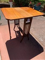 Full view of antique wooden end table outdoors showcasing the drop leaf extended sides and the wood grain tabletop surface.