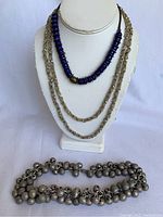 Front view of three necklaces displayed on a jewelry bust – blue glass beads, fine silver filigree chains, and silver tone clustered bead choker.