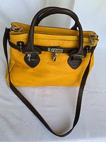 Front view of the yellow and dark brown leather handbag with handles, shoulder strap, and locking clasp key visible.